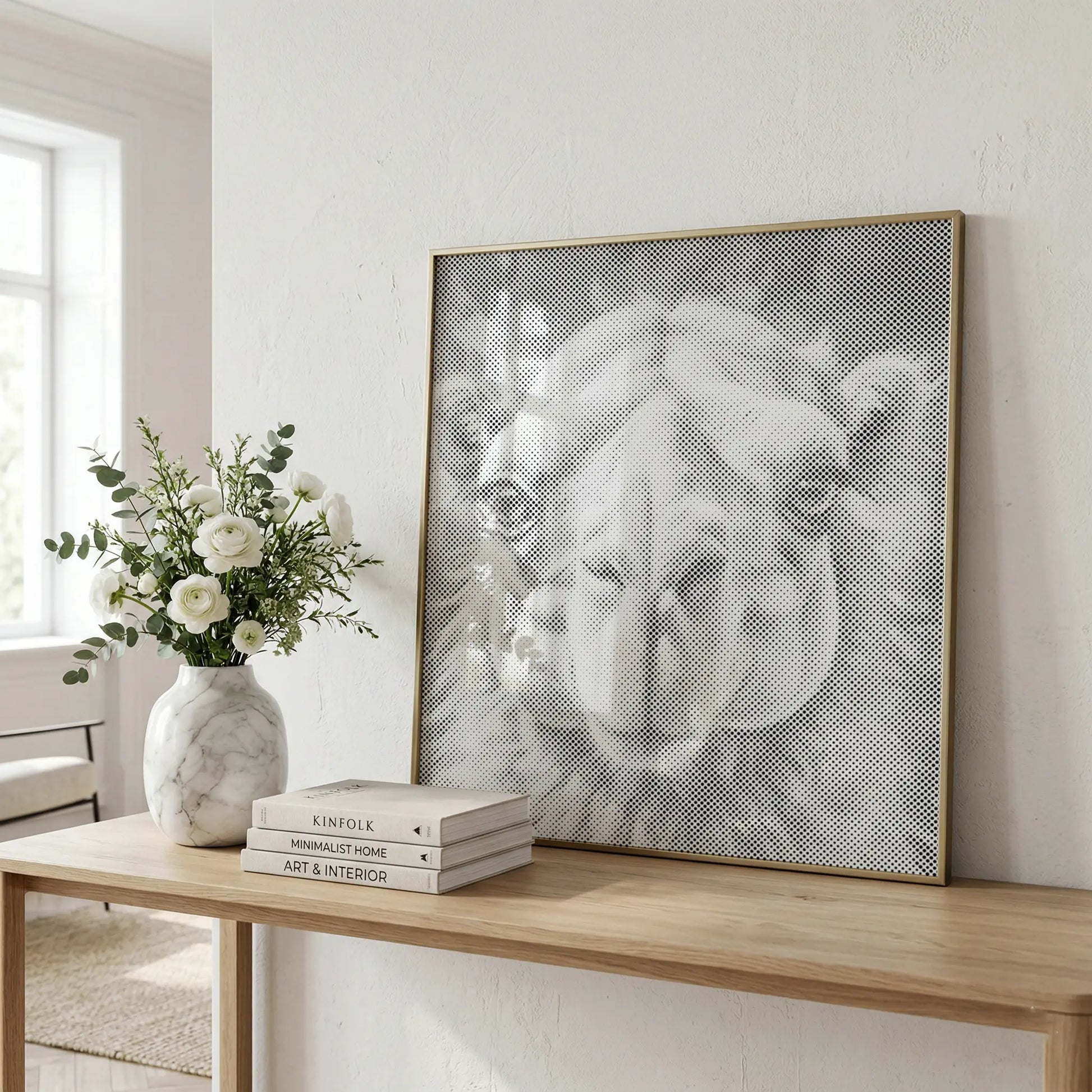 A large framed black and white canvas print of a camel's face leans against a white wall on a light wood console table, styled with a marble vase of white flowers and books.