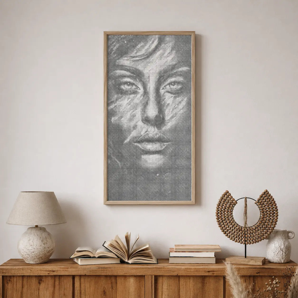 Framed artwork of a face on a wall above a wooden console table with books and decorative items. Face of Silence | Dot Painting Kit