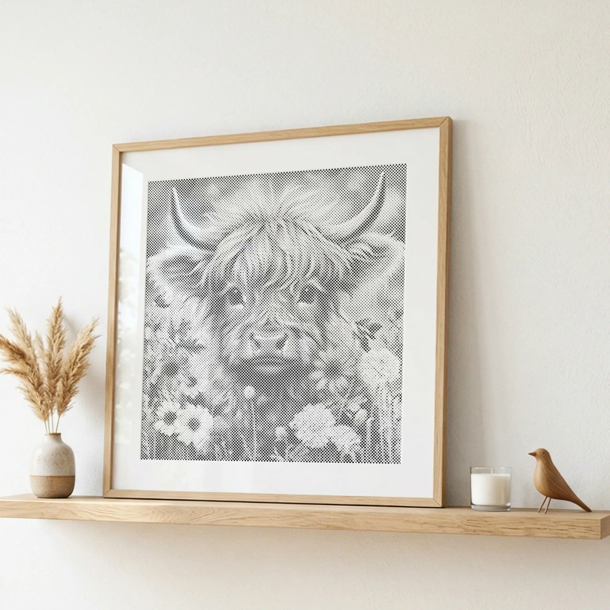 Framed artwork of a highland cow with flowers on a wooden shelf.