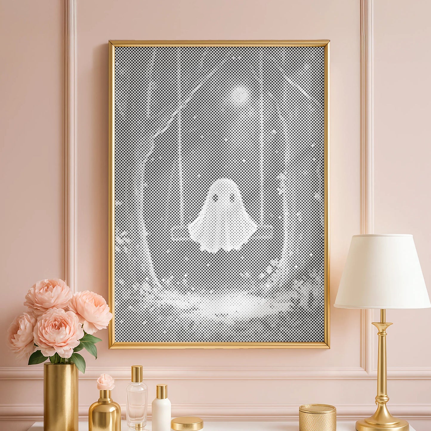 Decorative setup with a framed artwork of a ghost, flowers, and a lamp on a white surface against a pink wall.