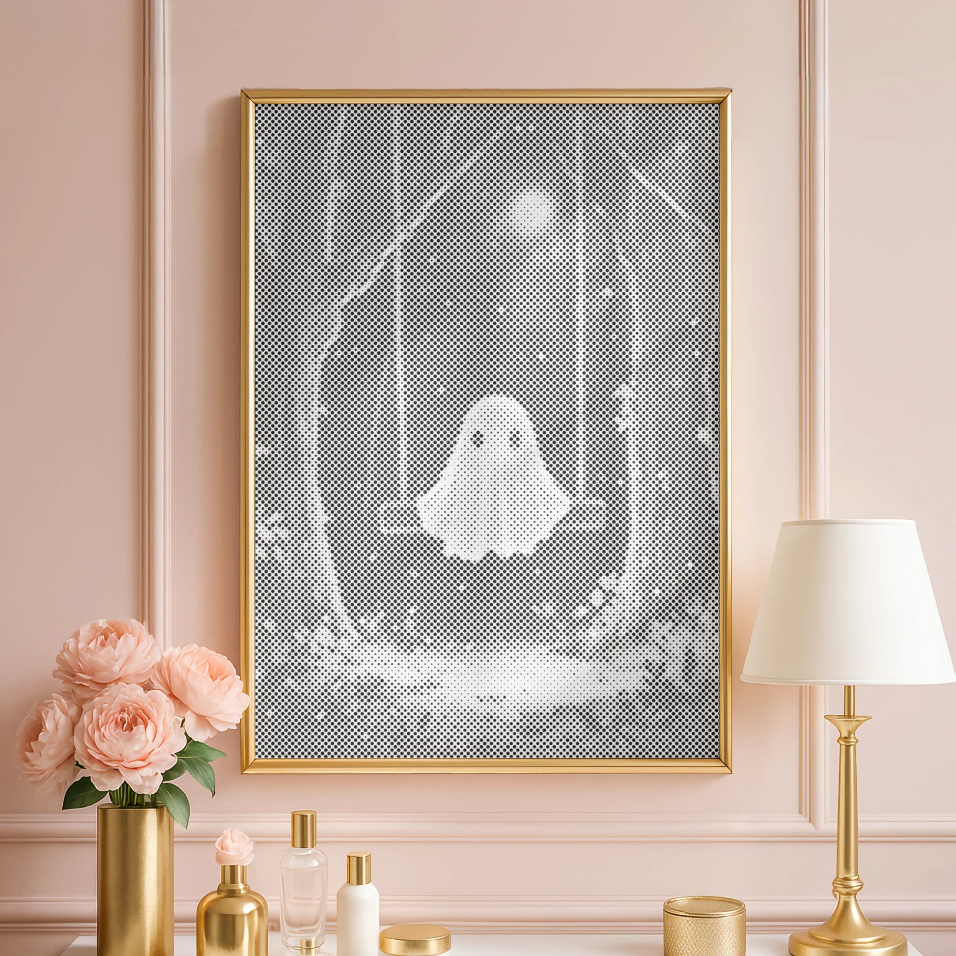 Decorative setup with a framed artwork of a ghost, flowers, and a lamp on a white surface against a pink wall.
